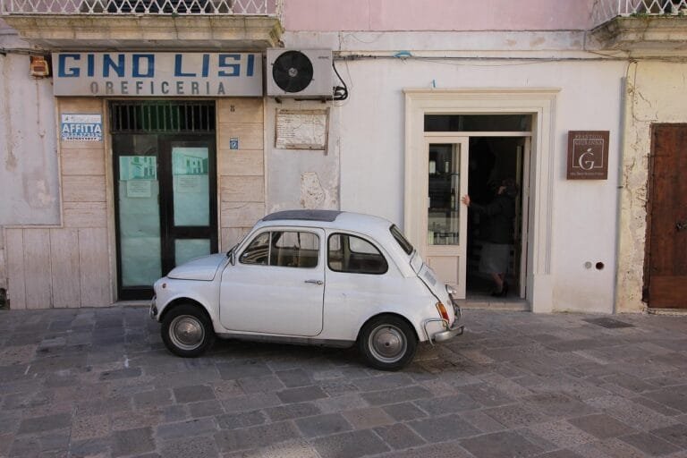 Louer une voiture dans les Pouilles : le meilleur guide ! 5 Fiat 500 garée dans une rue étroite d'un village blanc des Pouilles en Italie